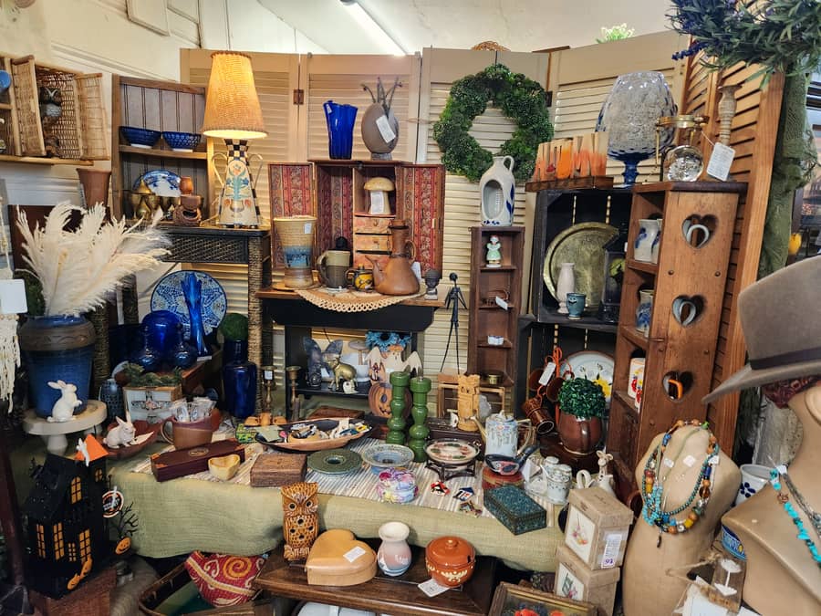 A dense vintage booth with a lamp, blue glassware, a wreath and wooden shelving