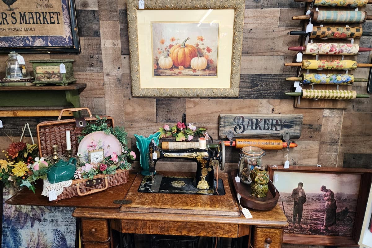 A vendor booth upstairs at Thieves Market with an antique treadle sewing machine, framed prints and a rack of painted rolling pins