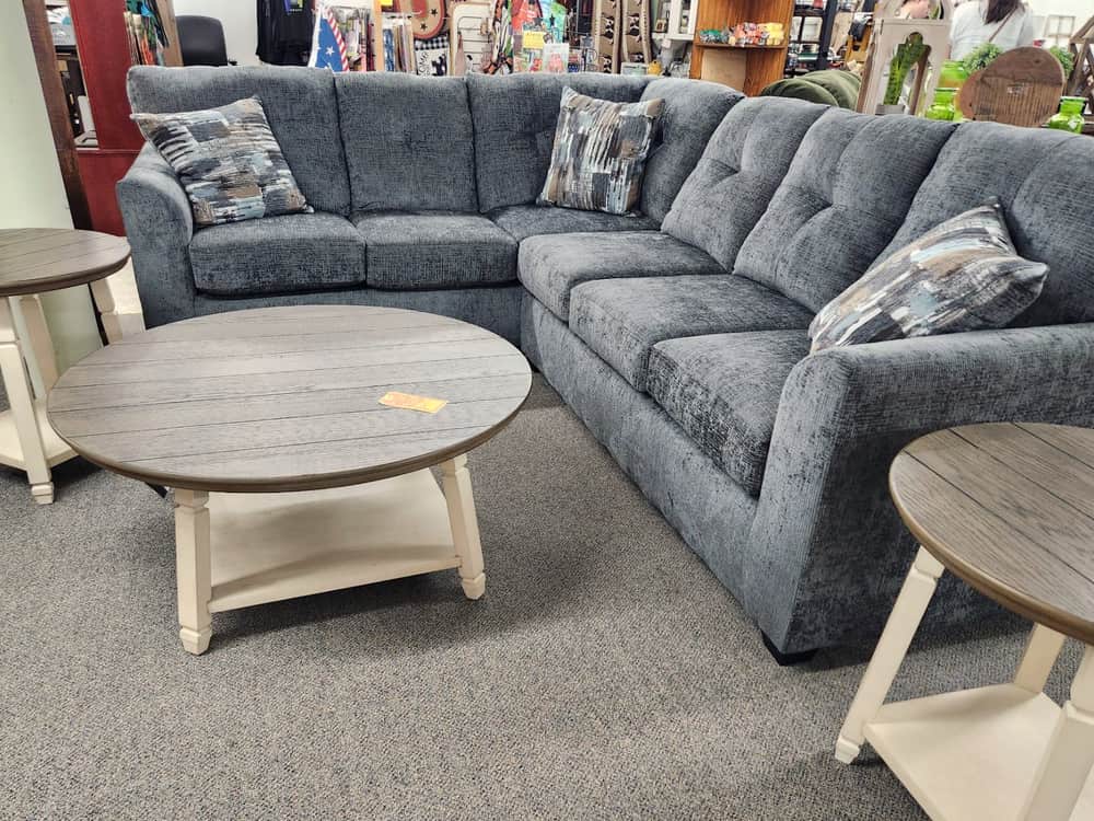 A blue grey tufted sectional with a round two tone coffee table