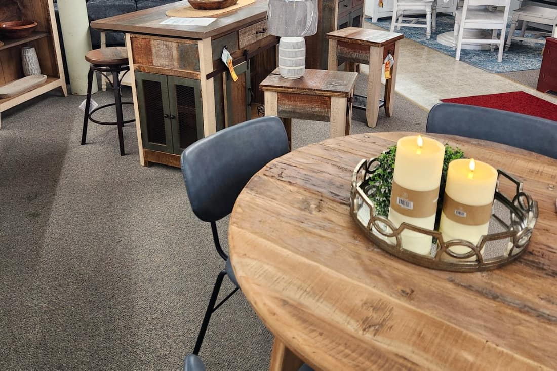 A round rustic wood dining table with navy upholstered chairs and three candles on a tray, on the first floor at Thieves Market