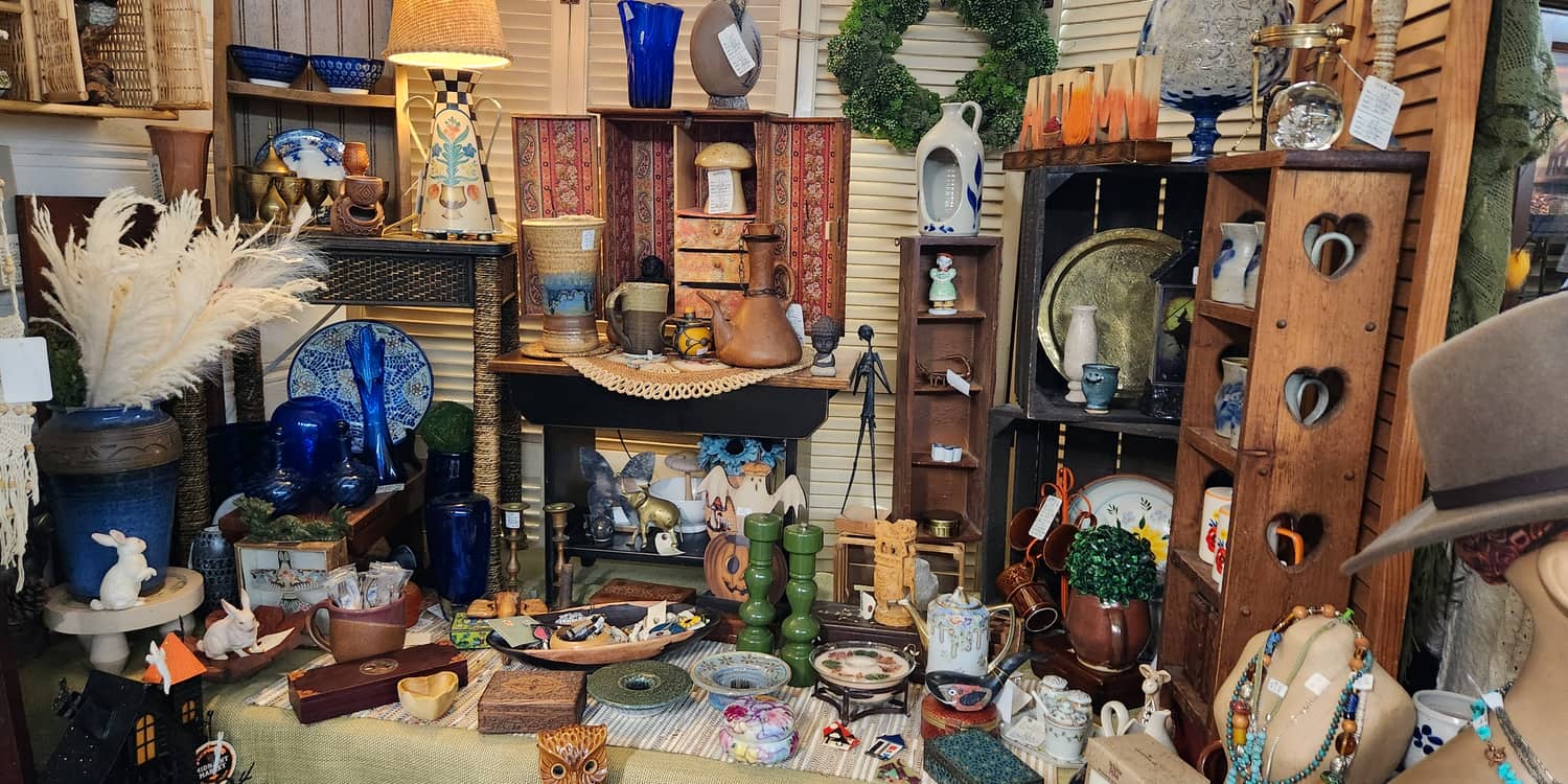 A dense vintage booth upstairs at Thieves Market with glassware, a lamp and a wreath