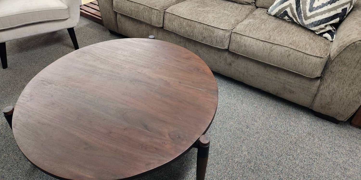 A taupe sofa with chevron cushions and a round wood coffee table at Thieves Market