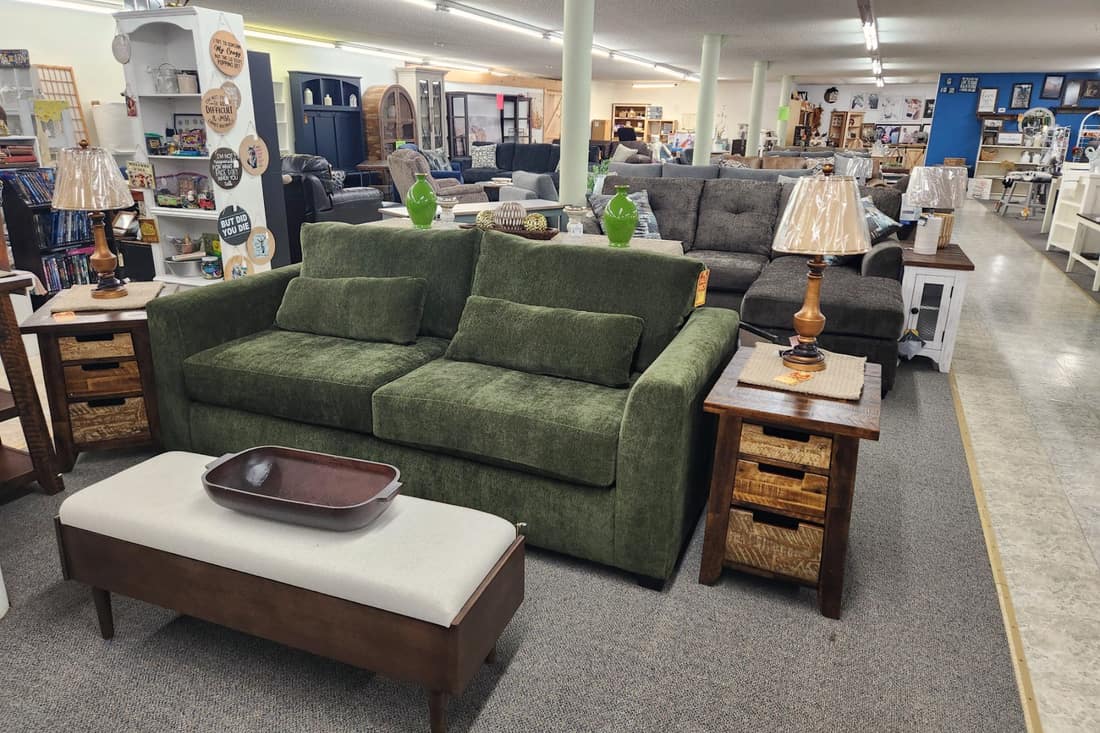 An olive green sofa with a cream upholstered bench and wood end tables on the Thieves Market first floor