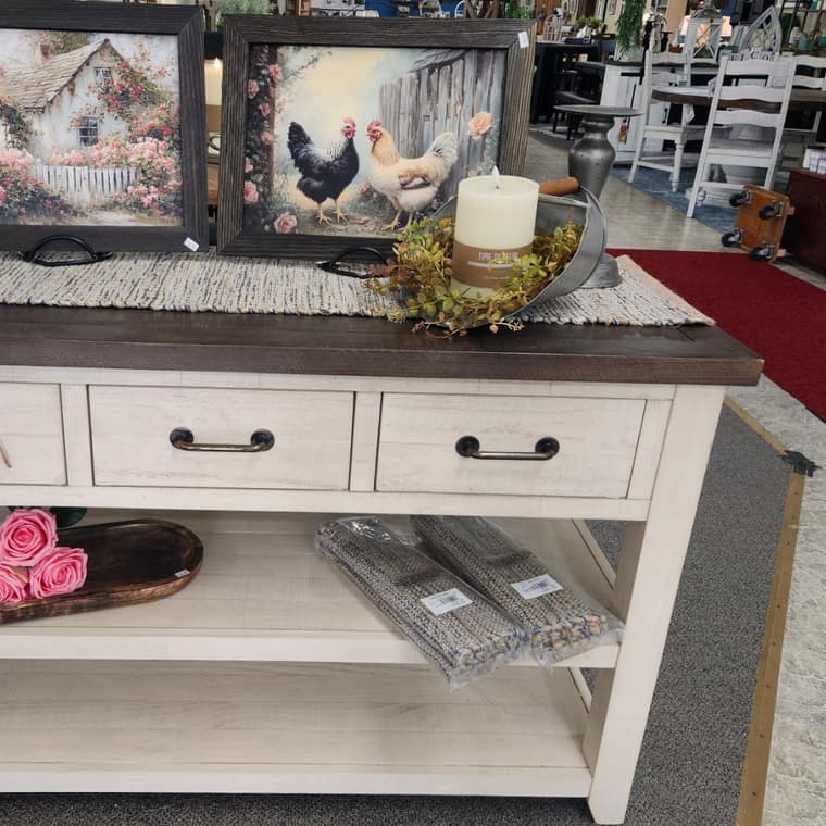 A cream console table styled with framed art, a candle and dried florals
