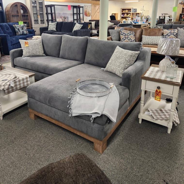 A blue grey tufted sectional with a round two tone coffee table
