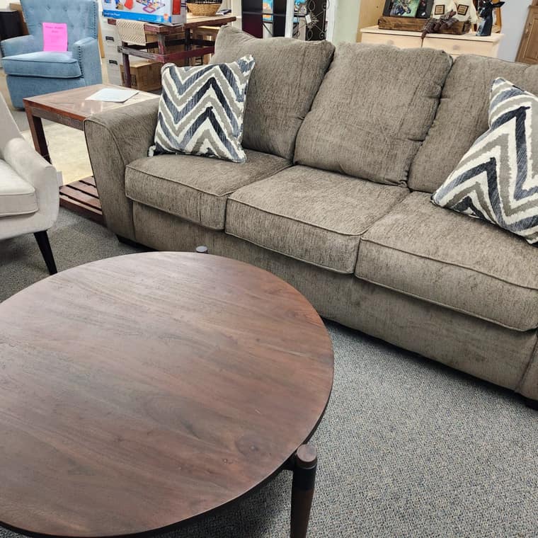 A round dark wood coffee table in front of a tan upholstered sofa