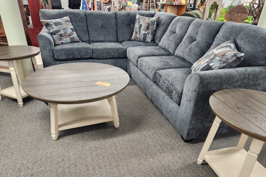 A blue grey tufted sectional with a round two tone coffee table at Thieves Market